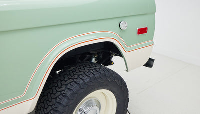 Rear fender and tire of porcelain green classic Ford Bronco with white and orange trim