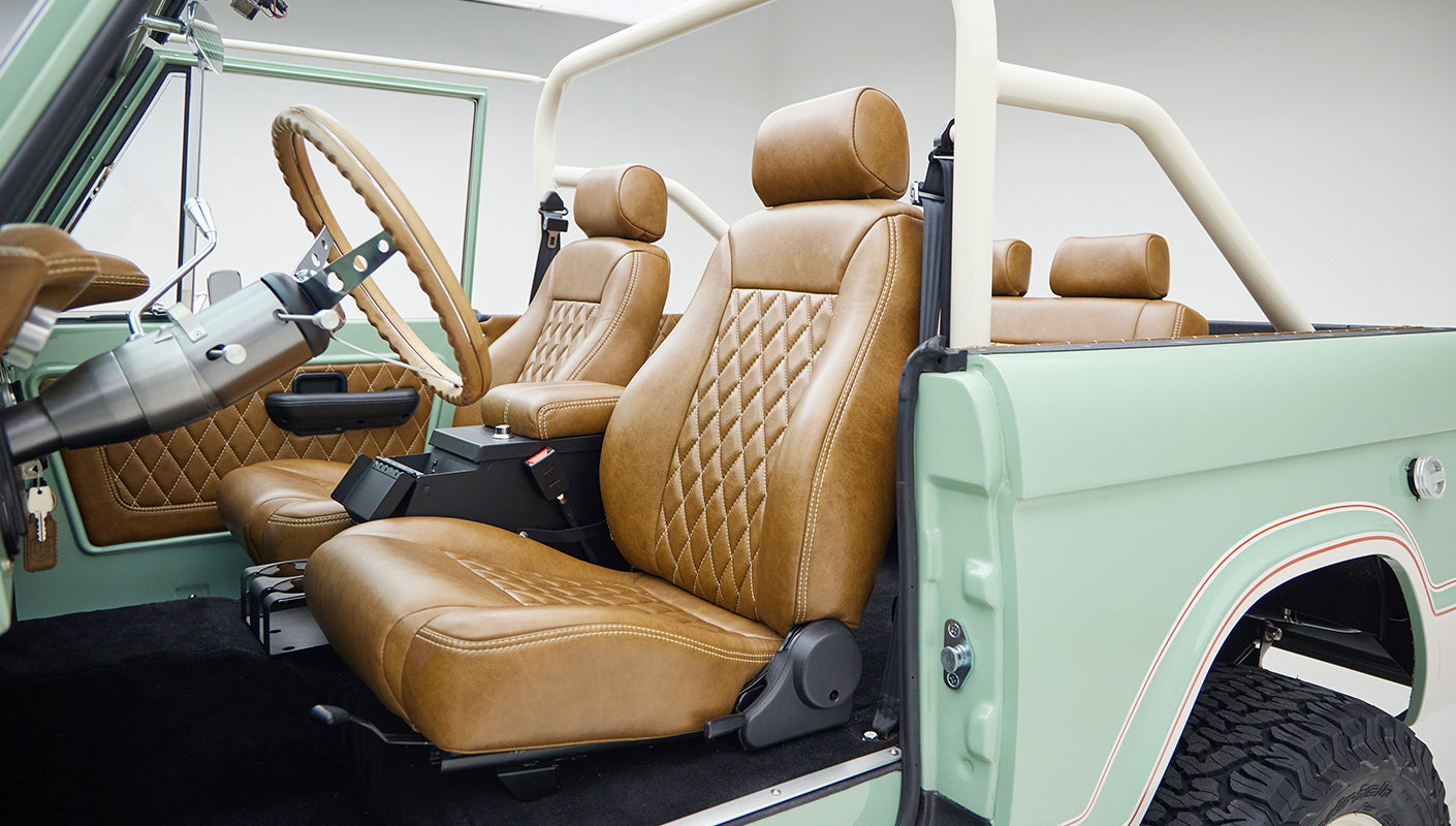 Interior of classic Ford Bronco featuring tan leather bucket seats and roll cage