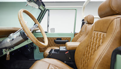 Driver's side interior of classic Ford Bronco with tan leather seats, steering wheel, and door panel