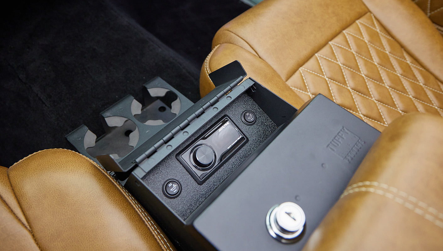 Center console inside classic Ford Bronco with audio controls, cup holders, and tan leather seats