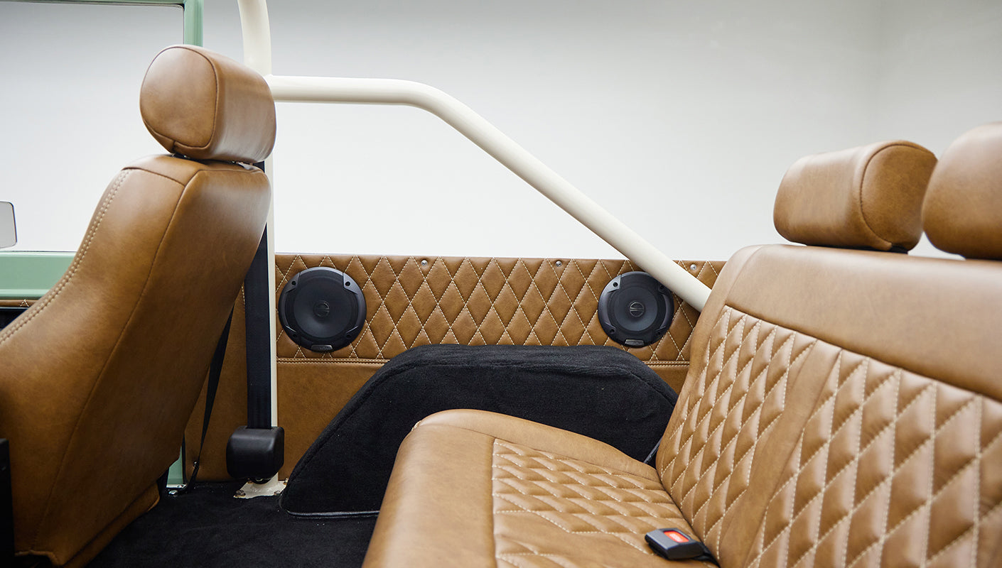 Side and rear interior view showing brown leather upholstery with diamond stitching and speakers