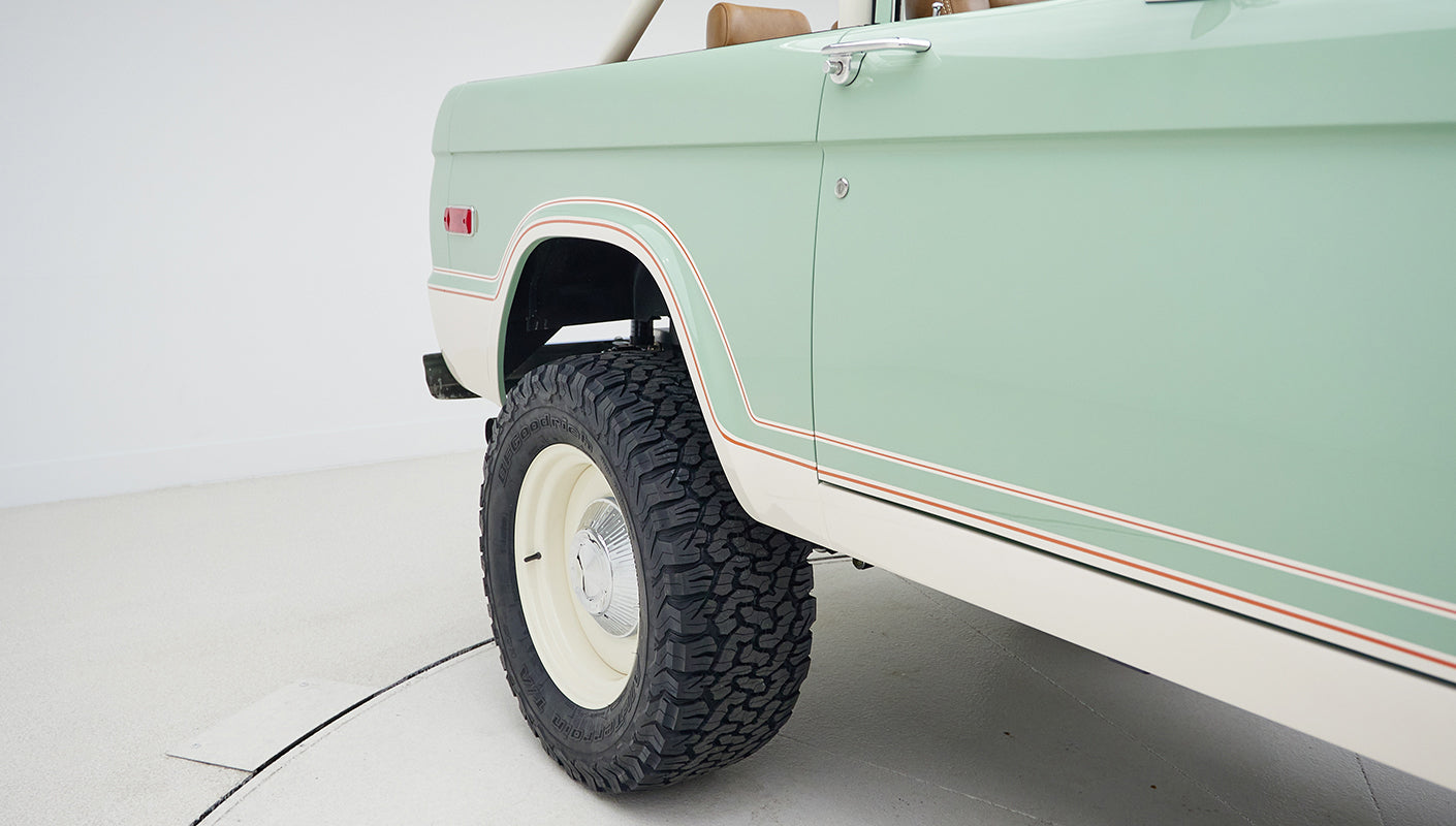 Close-up of rear wheel and pale green body panel with white and red trim on Classic Ford Bronco