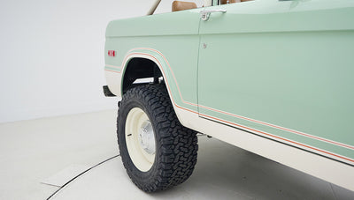 Close-up of rear wheel and pale green body panel with white and red trim on Classic Ford Bronco