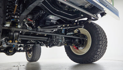 Undercarriage view showing suspension and axle of vehicle with off-road tires and light beige rims