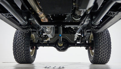 Undercarriage front view showing axle and suspension components with off-road tires and light beige rims