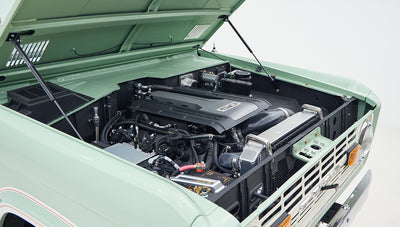 Open hood view of engine compartment with 5.0 badge and modern engine parts inside a light green vehicle