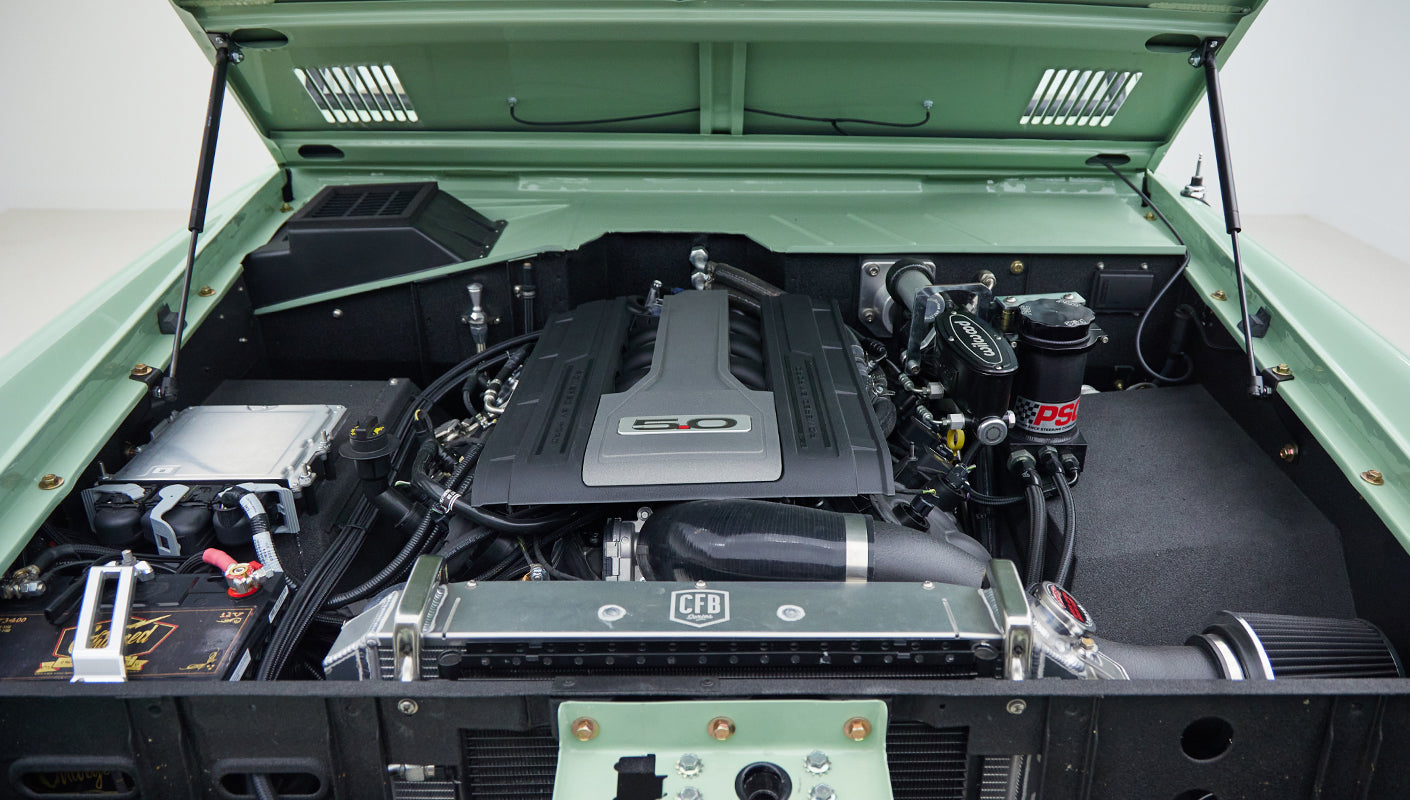 Engine compartment showing modern 5.0 liter engine and components inside a restored vehicle with light green paint
