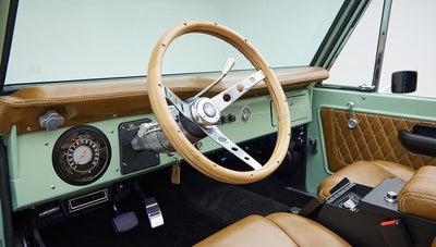 Dashboard of Classic Ford Bronco with porcelain green interior and tan leather steering wheel and seats.