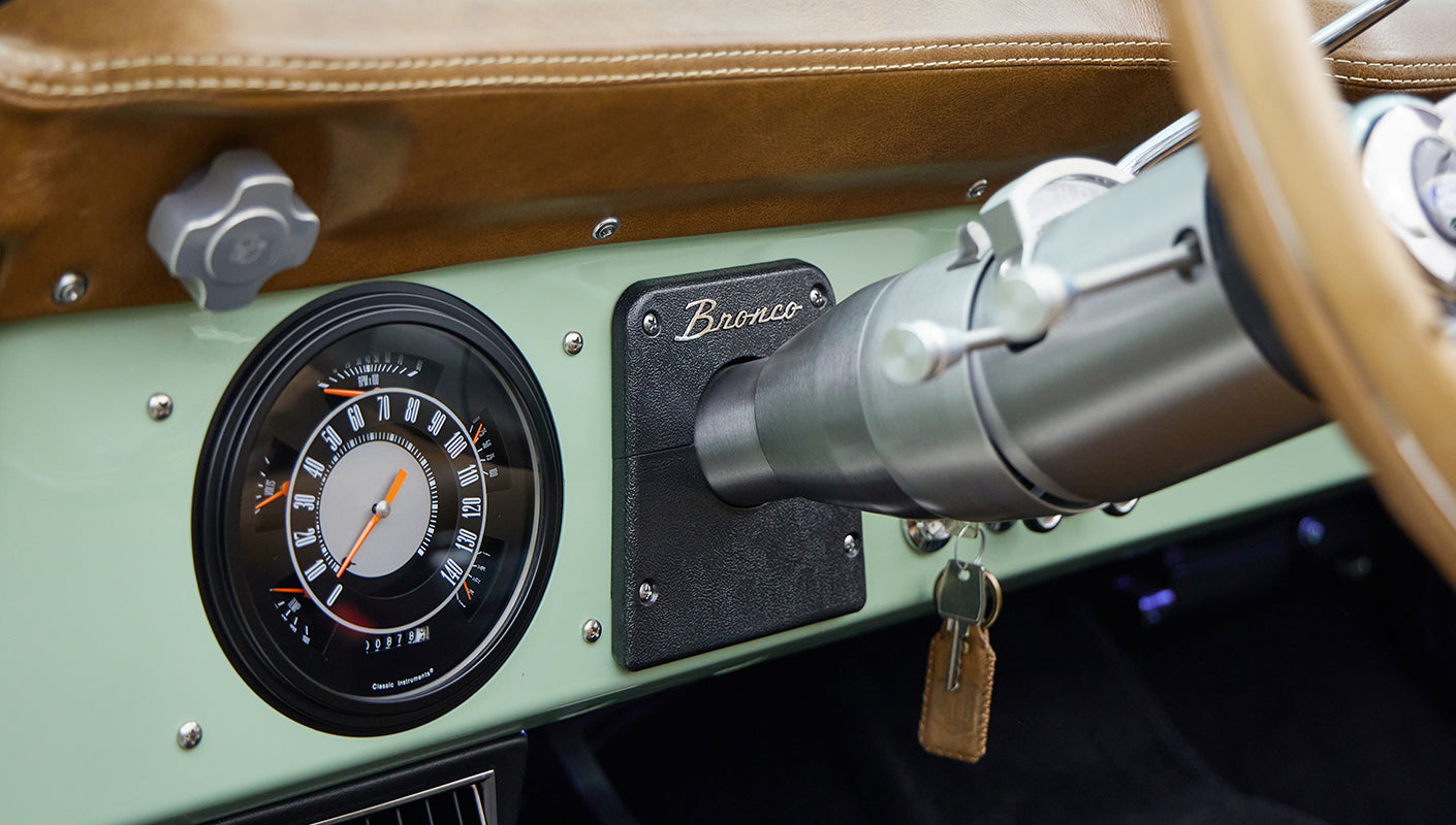 Close-up of Classic Ford Bronco dashboard showing round speedometer and ignition key with leather fob.