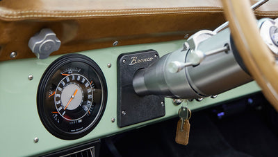 Close-up of Classic Ford Bronco dashboard showing round speedometer and ignition key with leather fob.