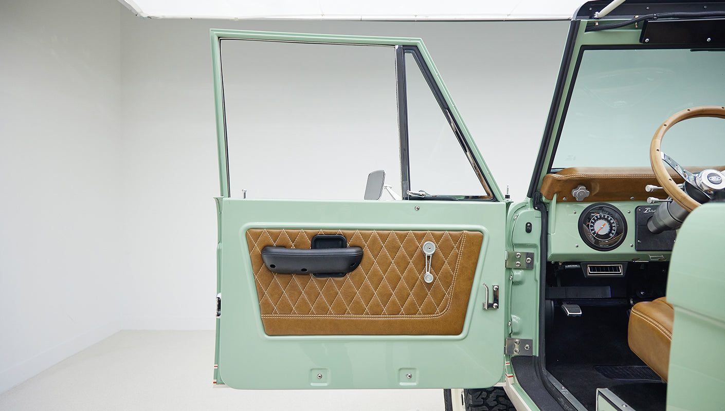 Open door of Classic Ford Bronco with porcelain green paint and tan leather quilted door panel.