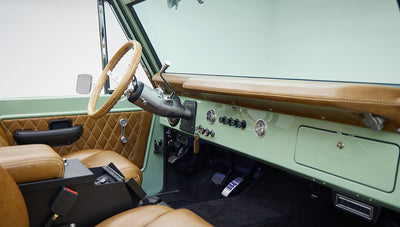 Interior of Classic Ford Bronco showing steering wheel, dashboard, and tan leather seats.