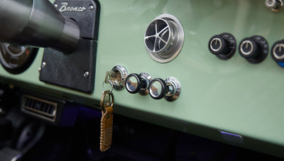 Close-up of ignition key with leather fob and control knobs on Classic Ford Bronco dashboard.
