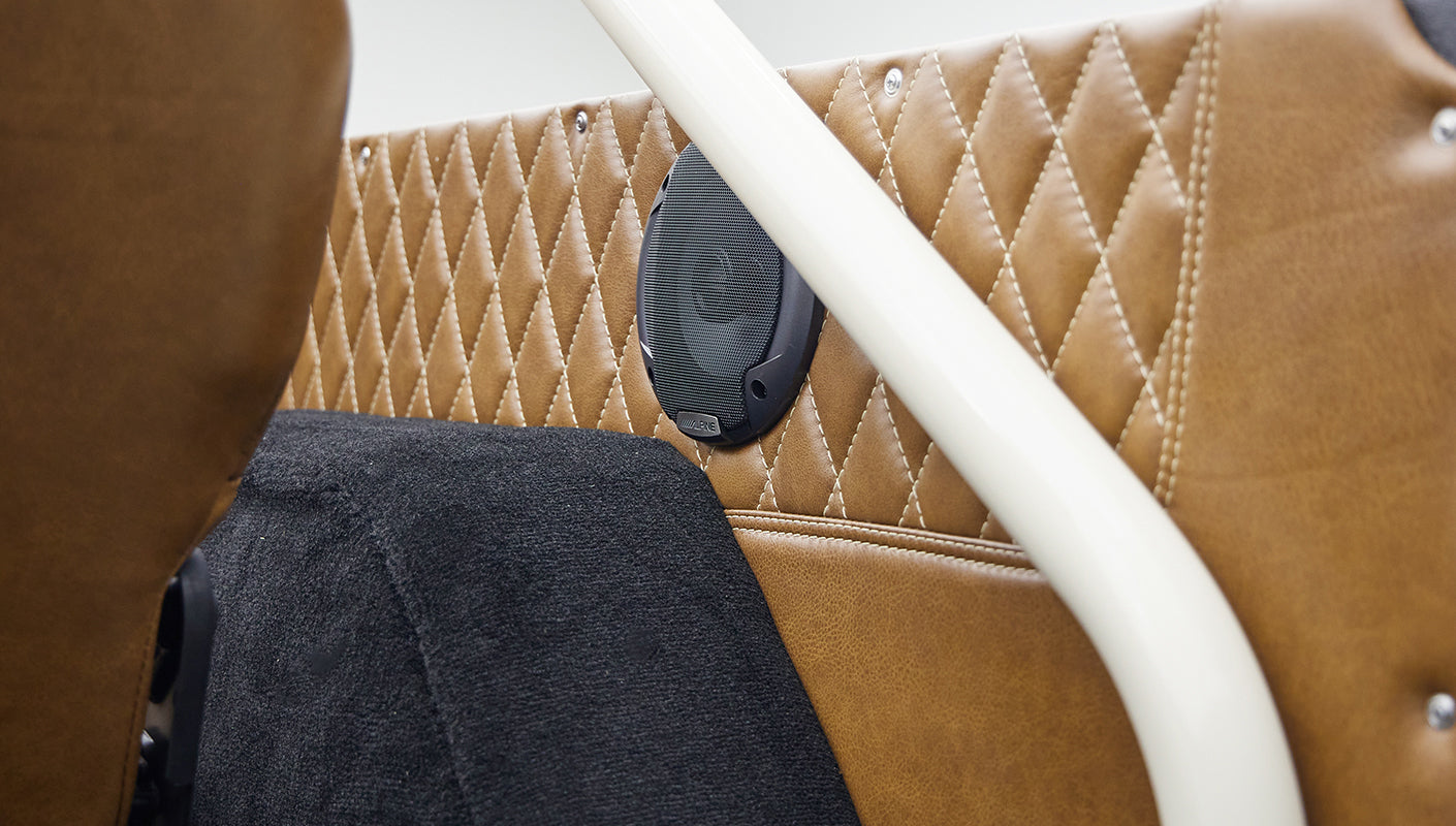 Tan quilted leather interior panel with mounted speaker and white roll cage in Classic Ford Bronco.