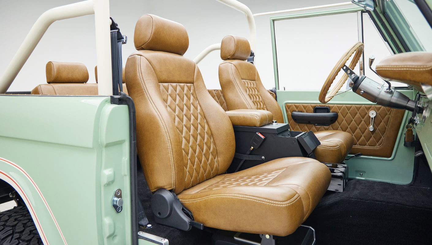 Front and rear tan leather seats inside Classic Ford Bronco with porcelain green doors and black carpet.
