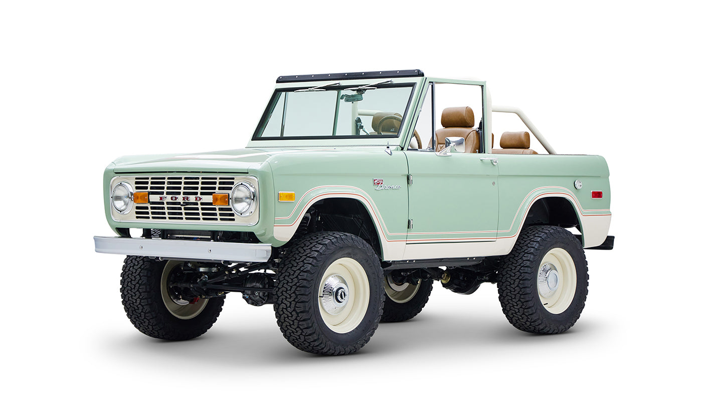 Front-side angle of mint green and cream Classic Ford Bronco with white rims and lifted suspension