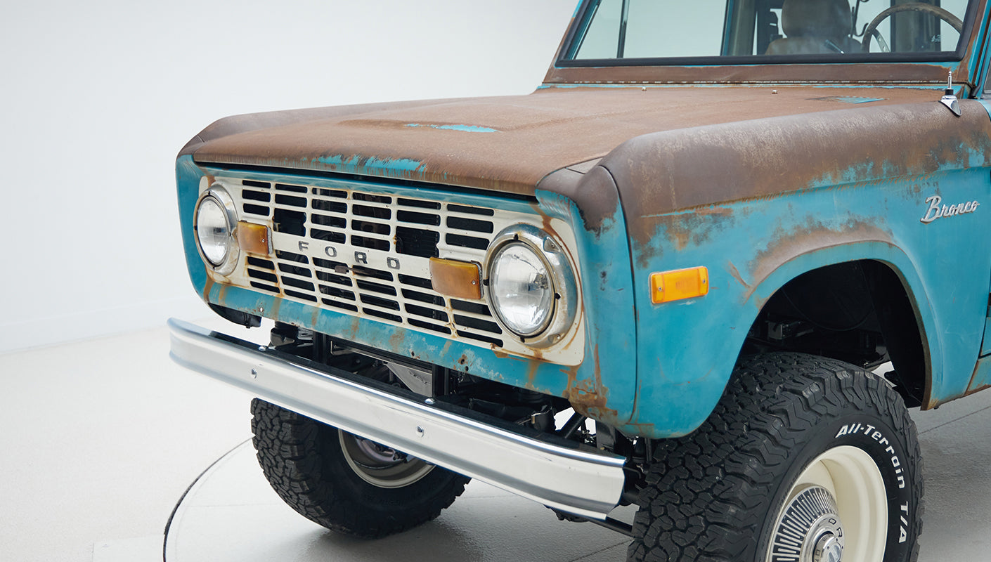 Close-up of front side of a turquoise Classic Ford Bronco showing rusted hood and front bumper.