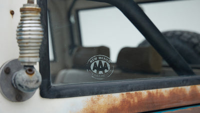 Rusty lower doorframe with AAA New Mexico sticker on window of Classic Ford Bronco