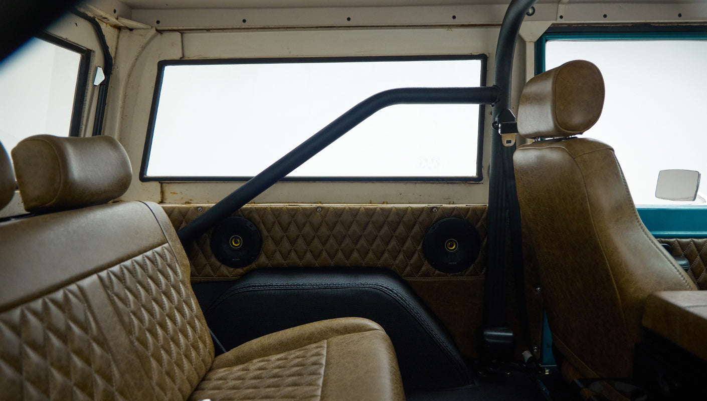 Classic Ford Bronco rear side view showing both front and rear brown leather seats and roll cage