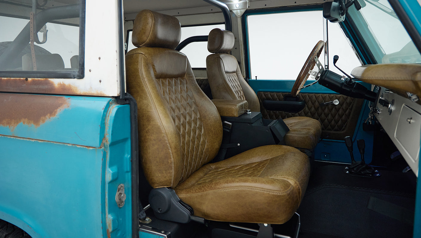 Side view of Classic Ford Bronco front interior showing brown leather seats and turquoise door