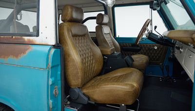 Side view of Classic Ford Bronco front interior showing brown leather seats and turquoise door