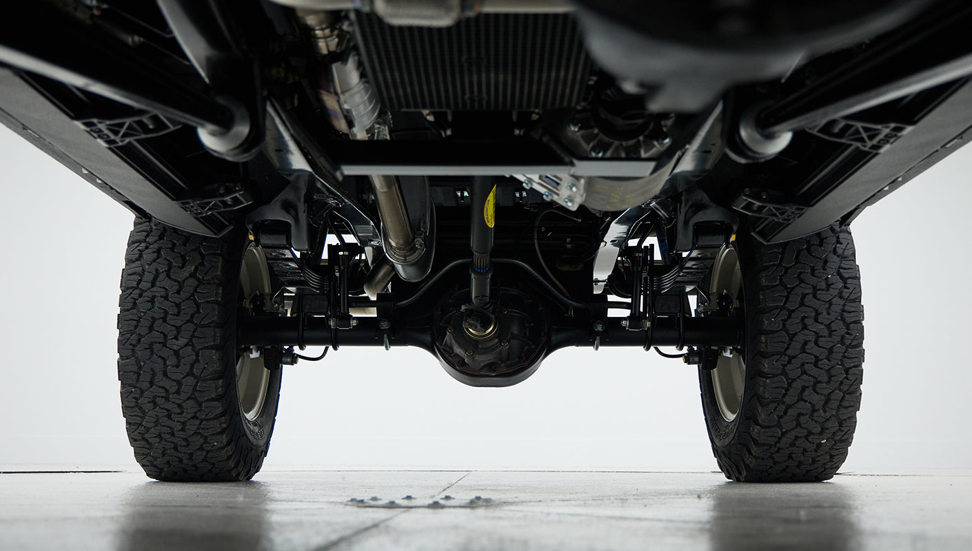 Underside view of a Classic Ford Bronco showing suspension and tires on a gray floor