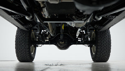Underside view of a Classic Ford Bronco showing suspension and tires on a gray floor