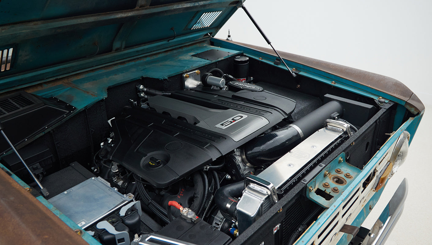 Engine bay of Classic Ford Bronco with black 5.0-liter engine and turquoise patina body