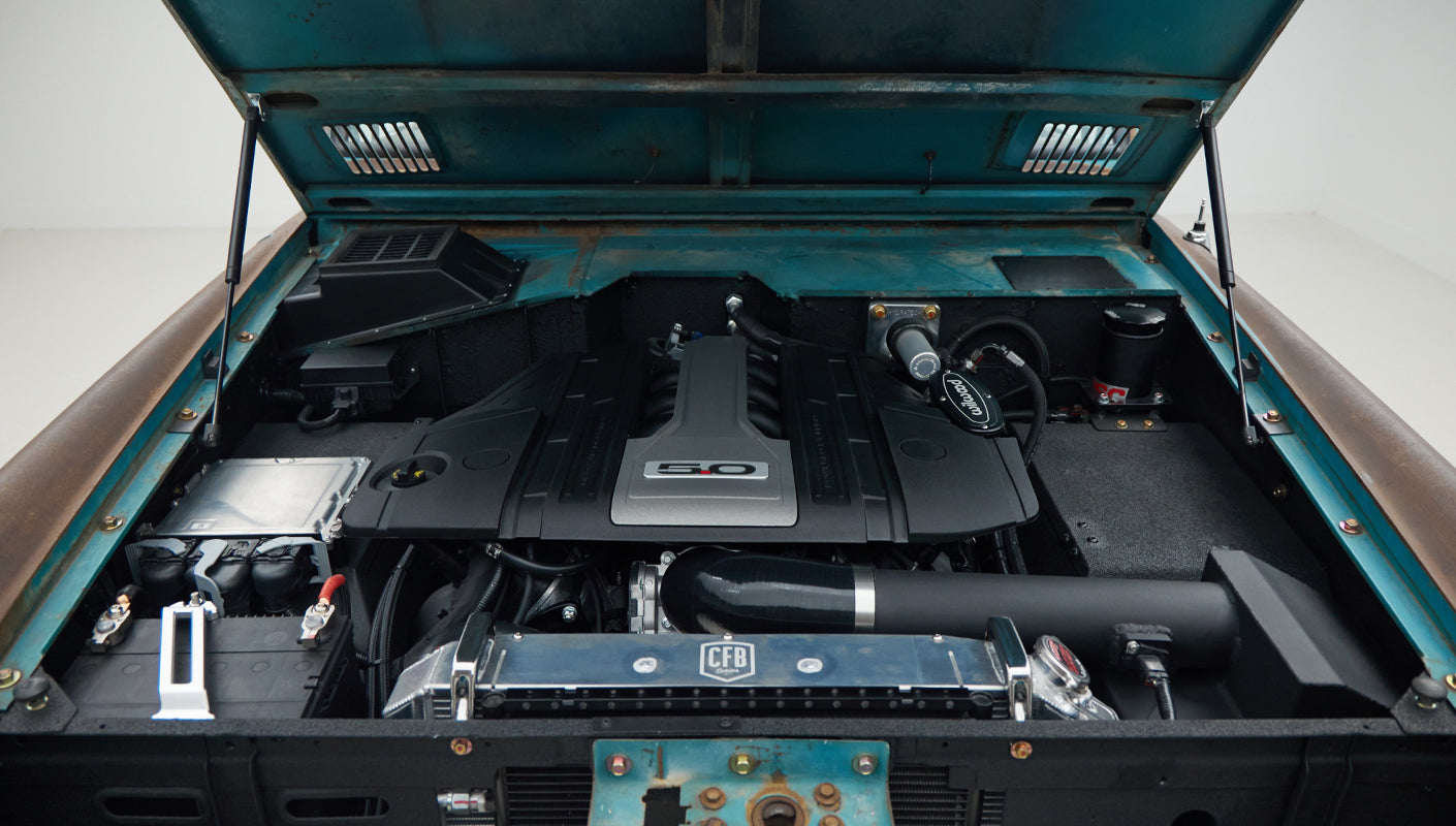 Close-up view of Classic Ford Bronco engine bay featuring black 5.0-liter engine and turquoise hood