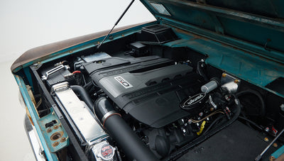 Another angle of Classic Ford Bronco engine bay with black 5.0-liter engine and patina turquoise body