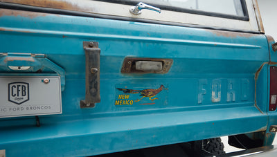 Close-up of rear door of Classic Ford Bronco in turquoise with faded New Mexico sticker and Ford embossed