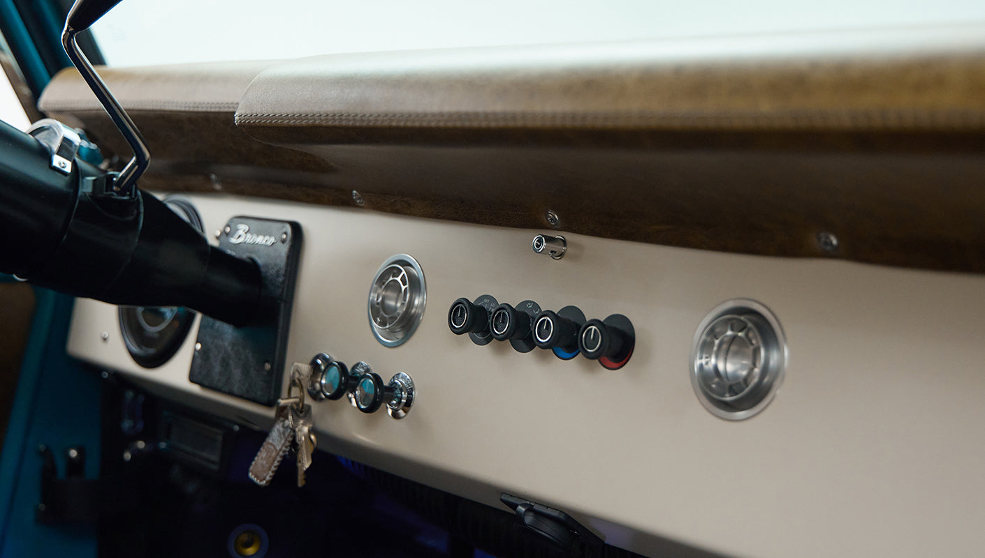 Dashboard close-up showing air vents, switches, keys, and tan leather interior of Classic Ford Bronco