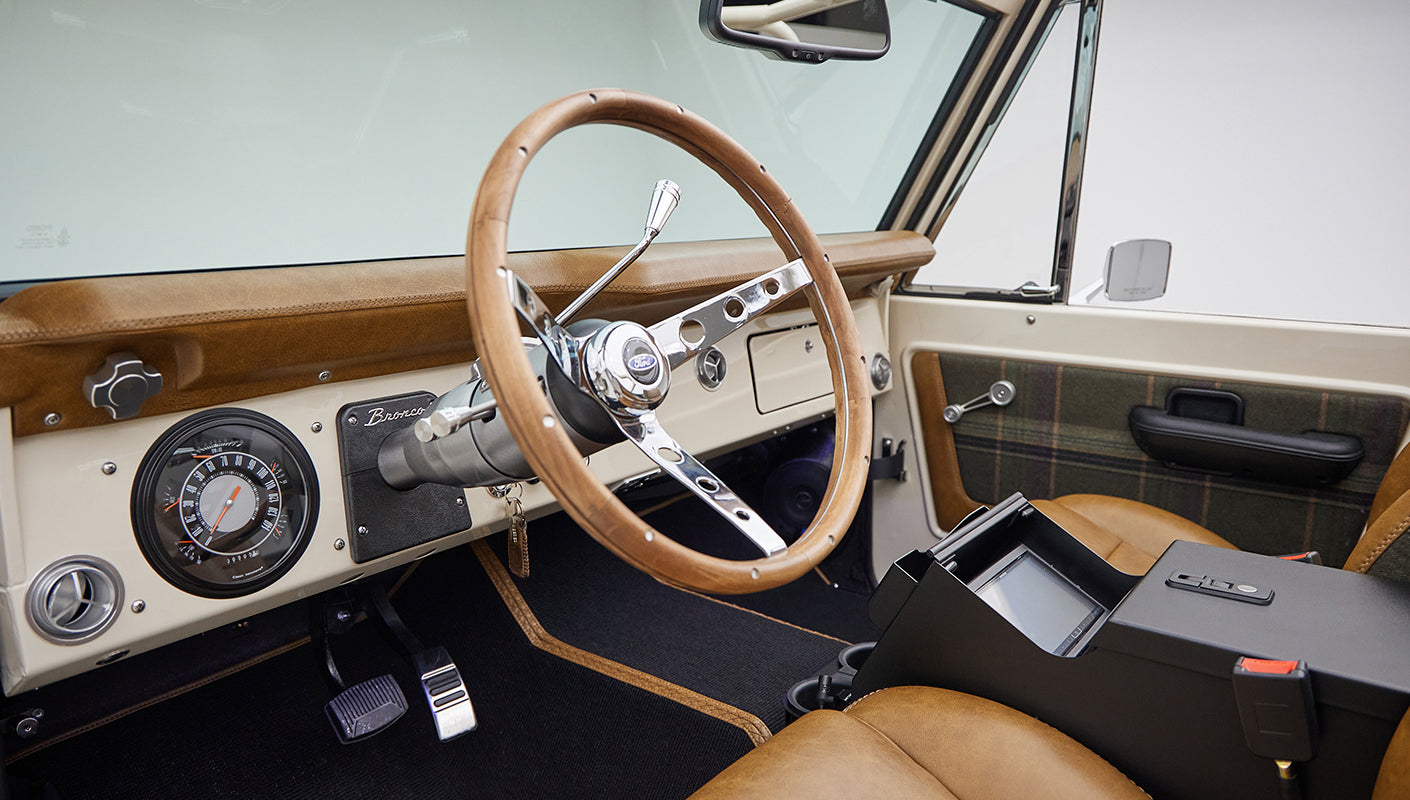 Driver area of Classic Ford Bronco featuring wooden steering wheel and plaid and leather seats