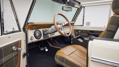 Driver's side interior of Classic Ford Bronco showing steering wheel and tan leather and plaid seats