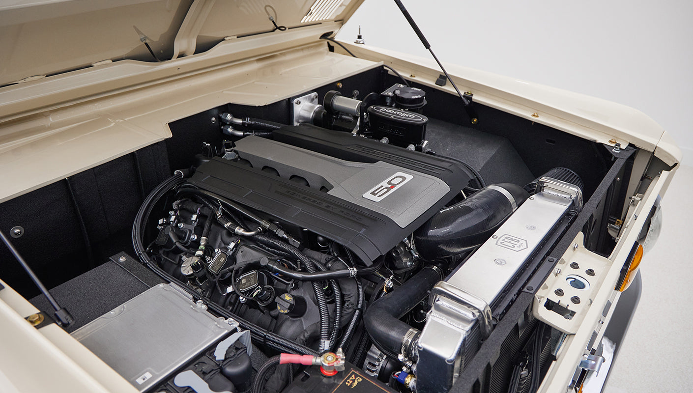 Open hood of Classic Ford Bronco showcasing a modern 5.0 engine with various components