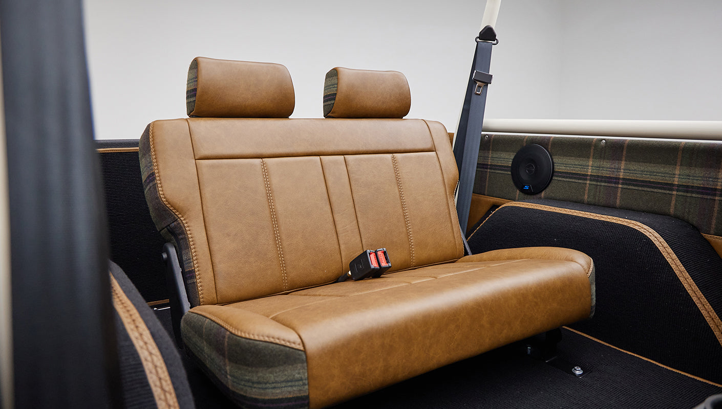 Rear seating area showing brown leather and plaid fabric, with two mounted speakers in Classic Ford Bronco