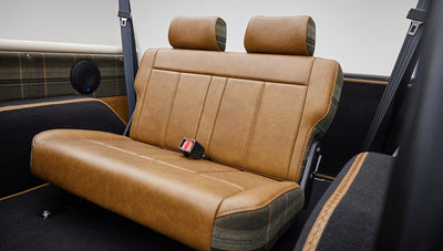 Rear bench seat inside Classic Ford Bronco in brown leather with plaid fabric accents and seat belts