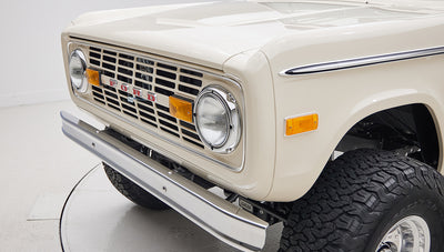 Front view of a cream-colored Classic Ford Bronco showing grille, headlights, and bumper