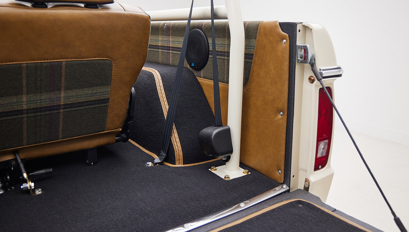 Rear interior area of Classic Ford Bronco with seat belts, speaker, and plaid upholstery