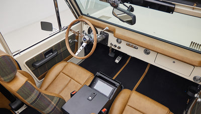 Classic Ford Bronco interior showing dashboard, steering wheel, and front seats with tan leather and plaid details