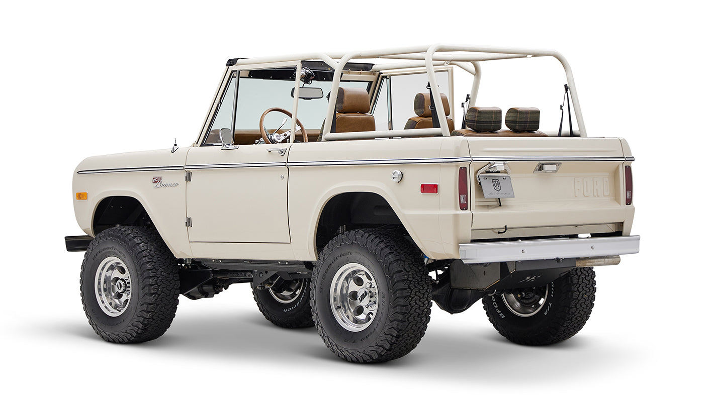 Classic Ford Bronco cream color with plaid rear seat covers shown from back-left angle on white background