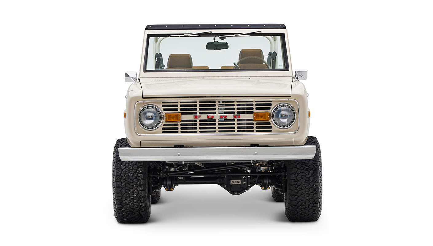 Classic Ford Bronco cream color front view showing grille, headlights, and large tires on white background
