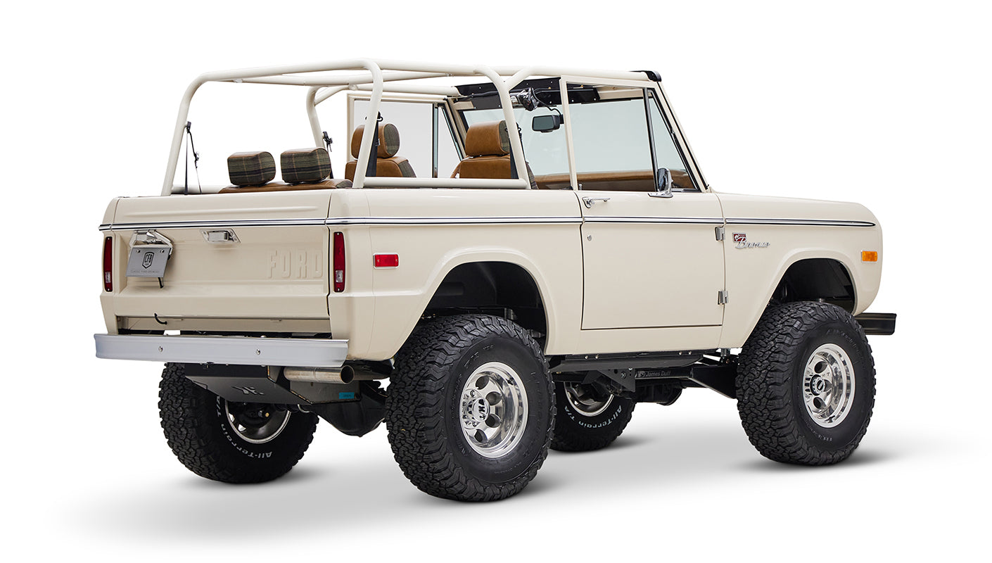 Classic Ford Bronco cream color with brown and plaid seats and open roof shown from back-right angle on white background
