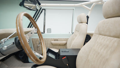 Classic Ford Bronco interior showing beige front seats, wood steering wheel, and dashboard from the driver side.