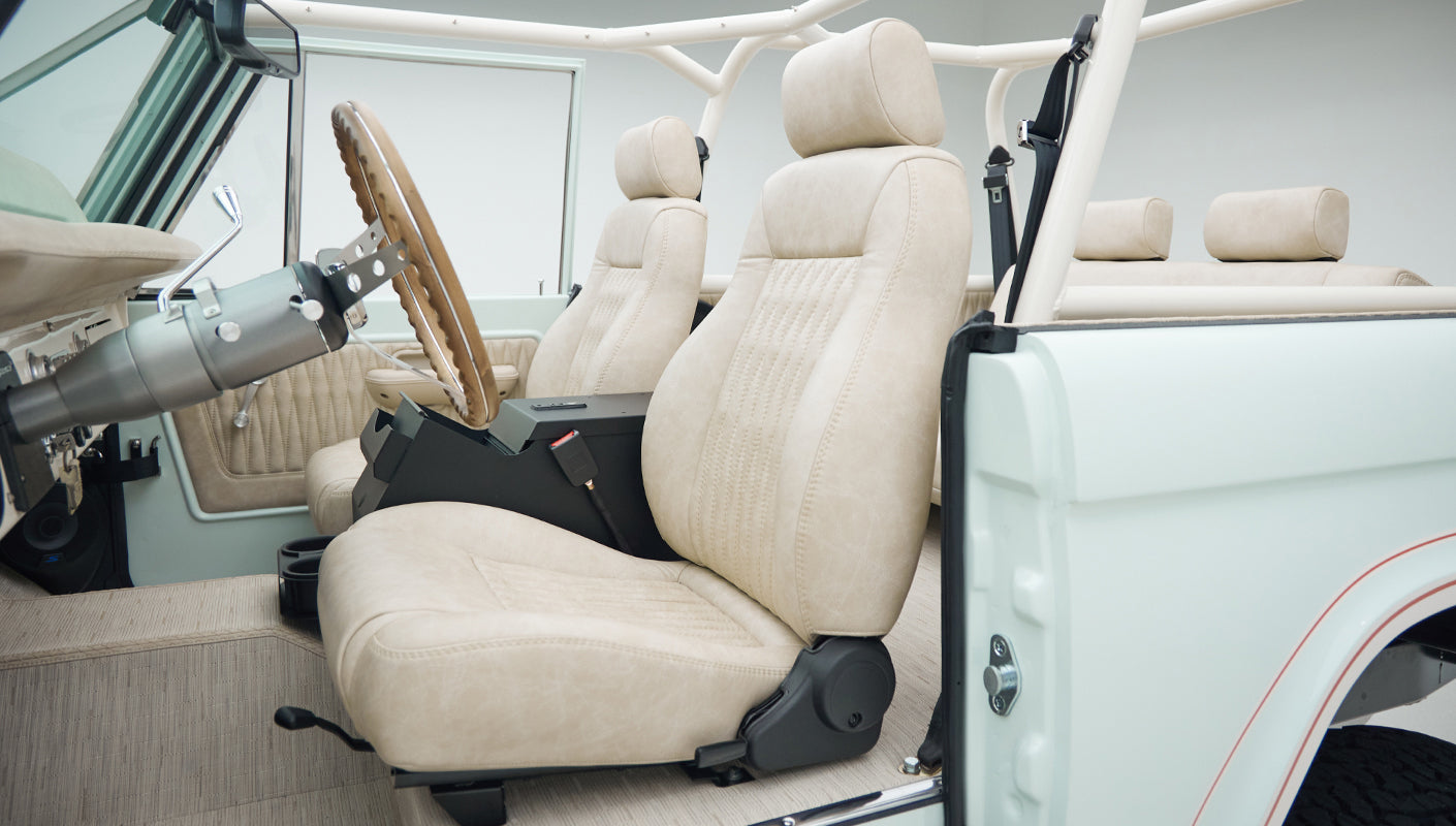 Interior side view of Classic Ford Bronco with beige seats and open door showing detailed upholstery and roll cage.