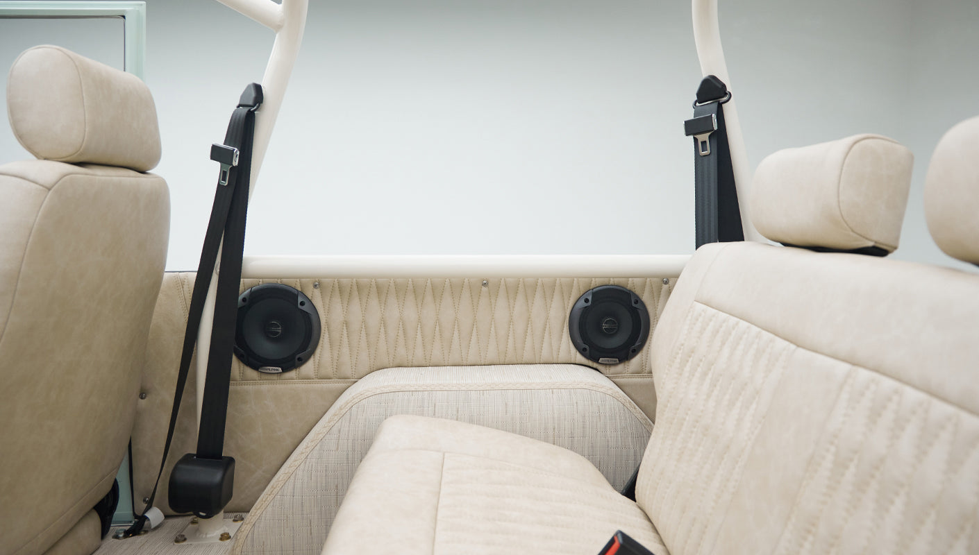 Side view of rear beige upholstered seat with seatbelts and built-in speakers in Classic Ford Bronco