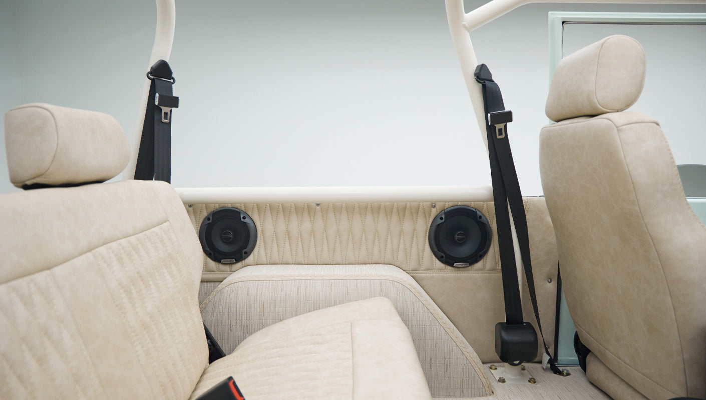 Second-row beige upholstered seats with two black seatbelts and speakers in Classic Ford Bronco interior