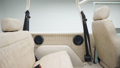 Second-row beige upholstered seats with two black seatbelts and speakers in Classic Ford Bronco interior