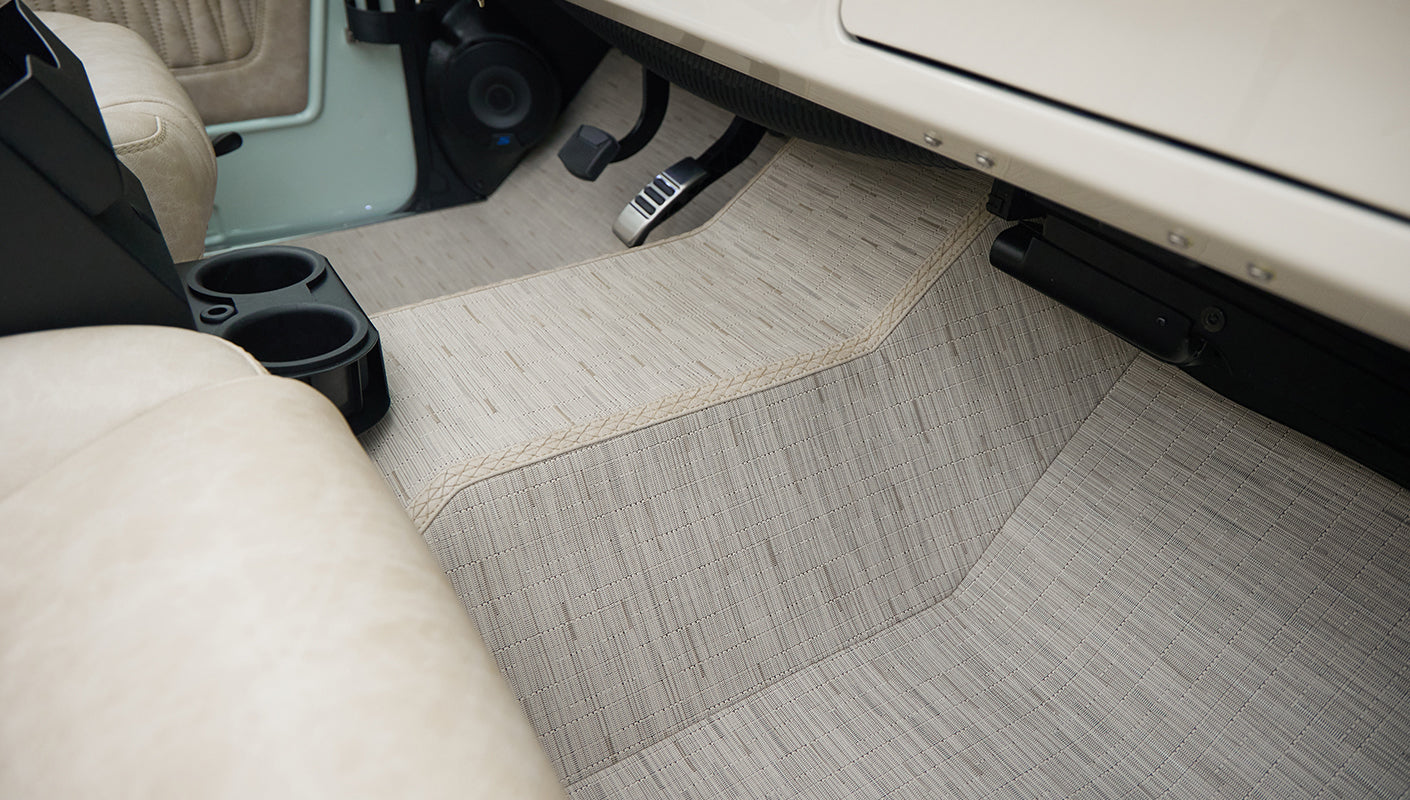 Floor board area with beige floor mats and black cup holder near front seats in Classic Ford Bronco