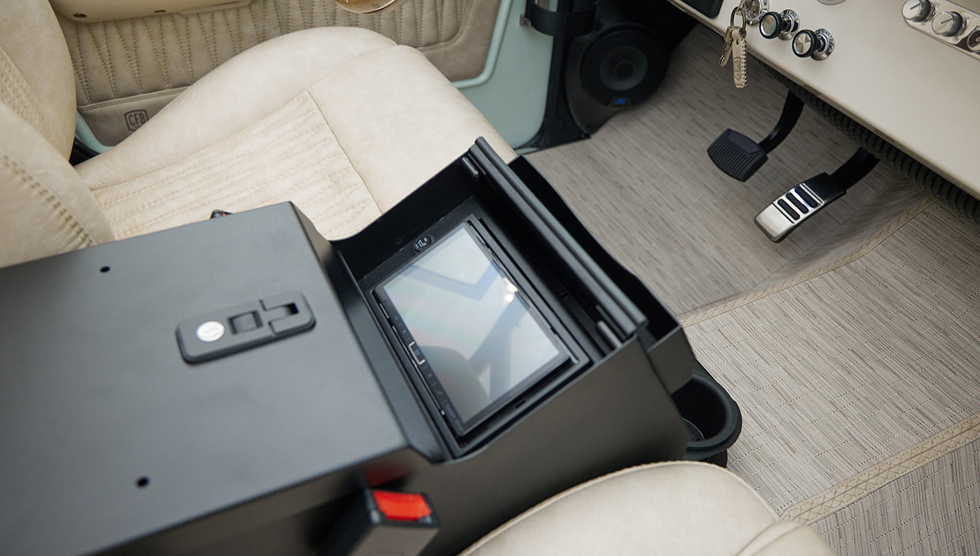 Open black center console compartment with a mounted screen above beige seat and floor mats in Classic Ford Bronco